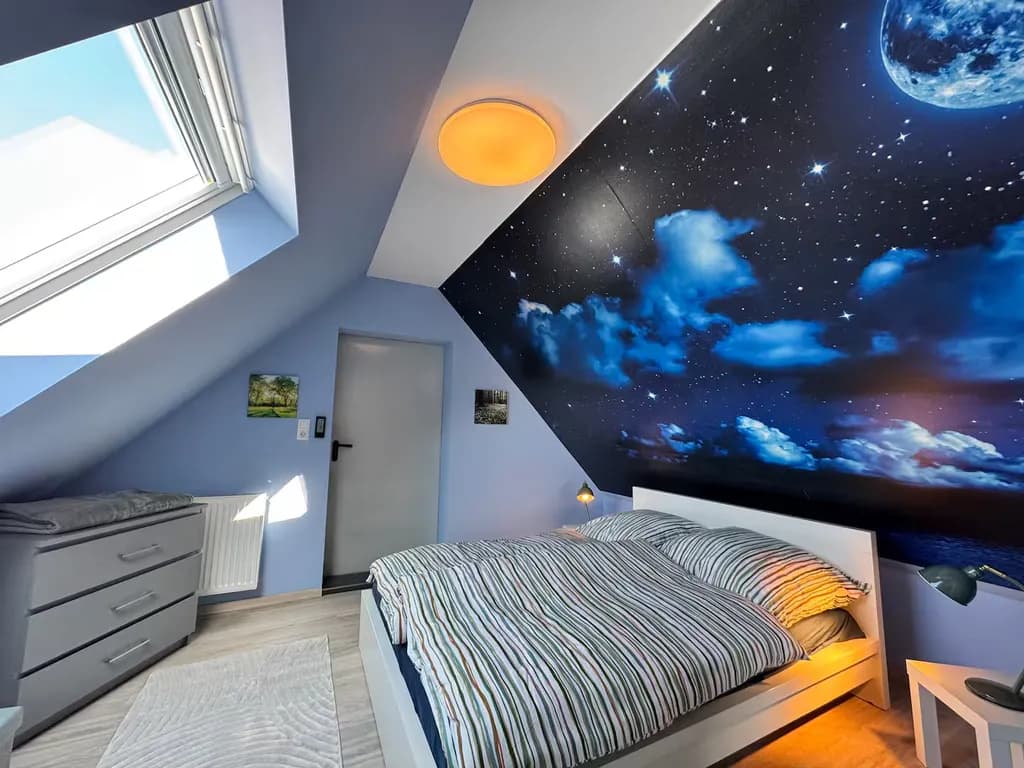 Schlafzimmer der Ferienwohnung mit Sternenhimmel-Fototapete und Dachfenster